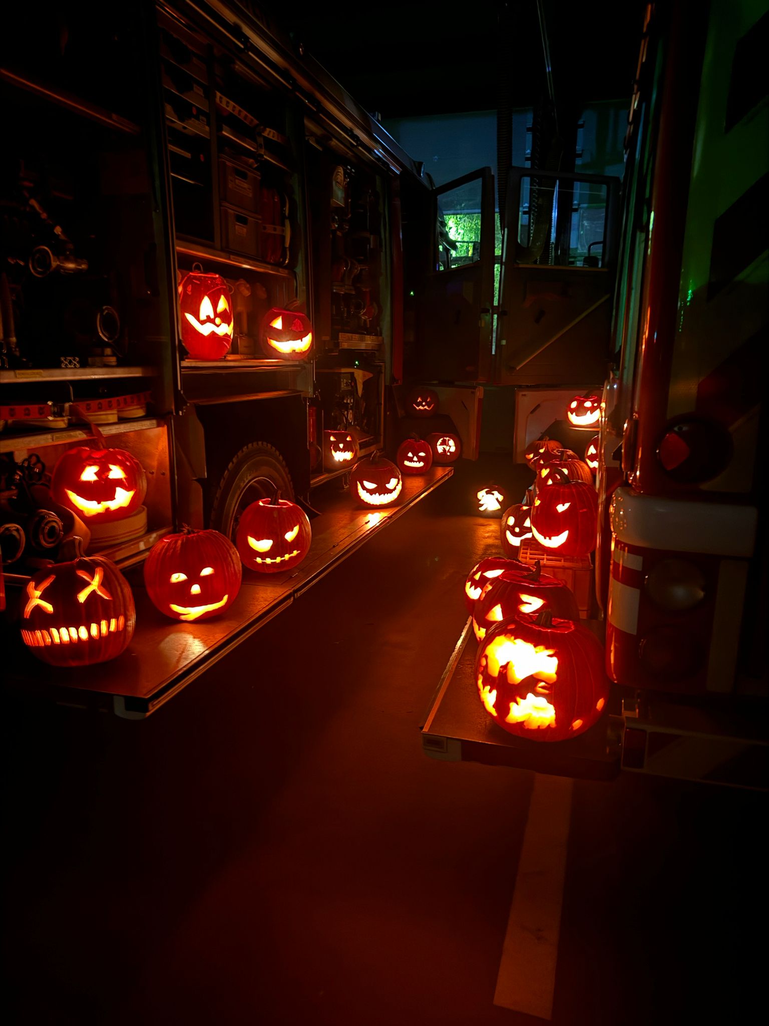 Es sind Halloweenkürbise zu sehen, die von innen, durch Kerzen beleuchtet, in der dunklen Fahrzeughalle aufgereiht sind.